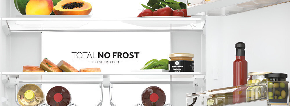 Wnętrze lodówki z półkami wypełnionymi różnymi produktami spożywczymi, takimi jak owoce, warzywa, słoiki i butelki. Na tylnej ściance widoczny jest napis \'TOTAL NO FROST FRESHER TECH\'.
