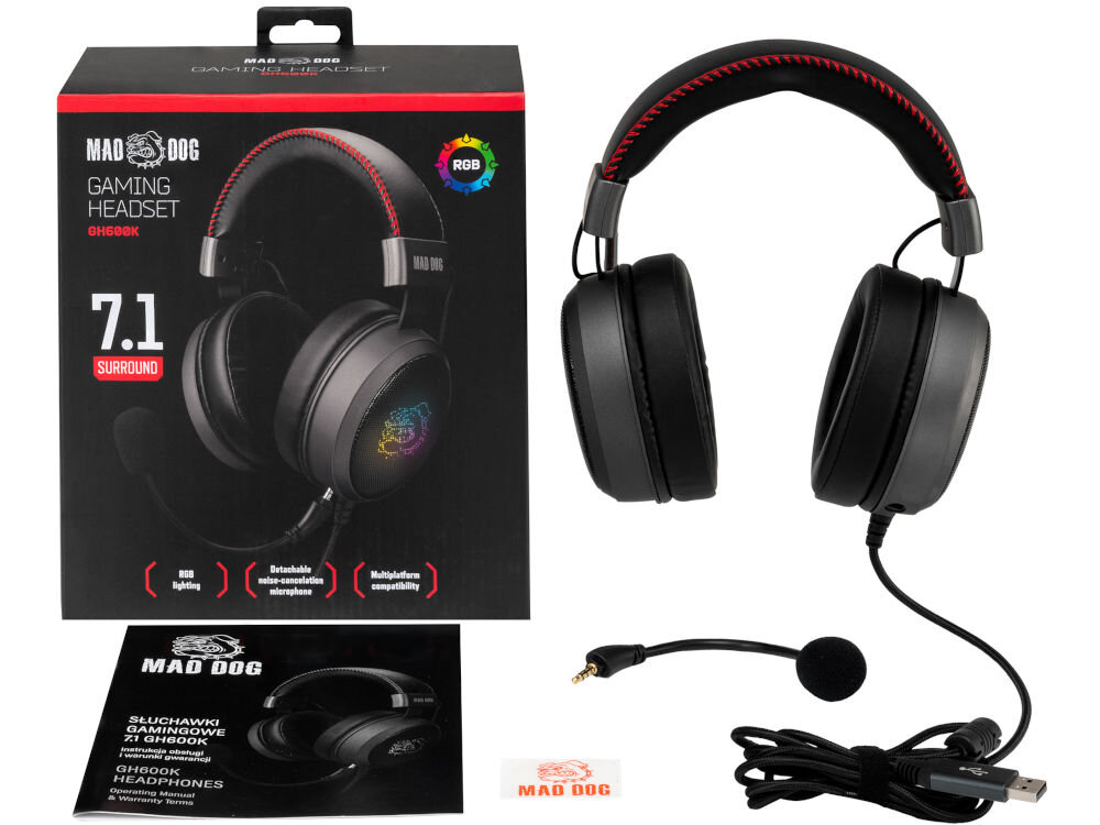Na obrazie widoczne są czarne słuchawki nauszne z czerwonymi akcentami oraz odłączanym mikrofonem. Obok znajduje się pudełko z napisem \'MAD DOG GAMING HEADSET GH600K 7.1 SURROUND\' oraz ulotka z logo MAD DOG.