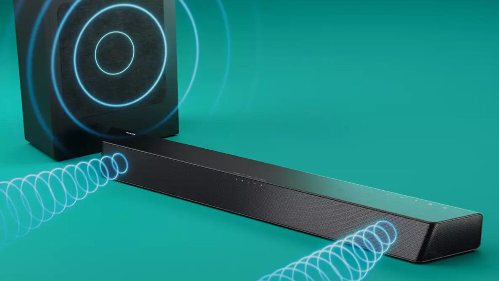 Czarny soundbar z widocznymi falami dźwiękowymi obok subwoofera na zielonym tle. Na soundbarze znajdują się małe, białe oznaczenia kontrolne.