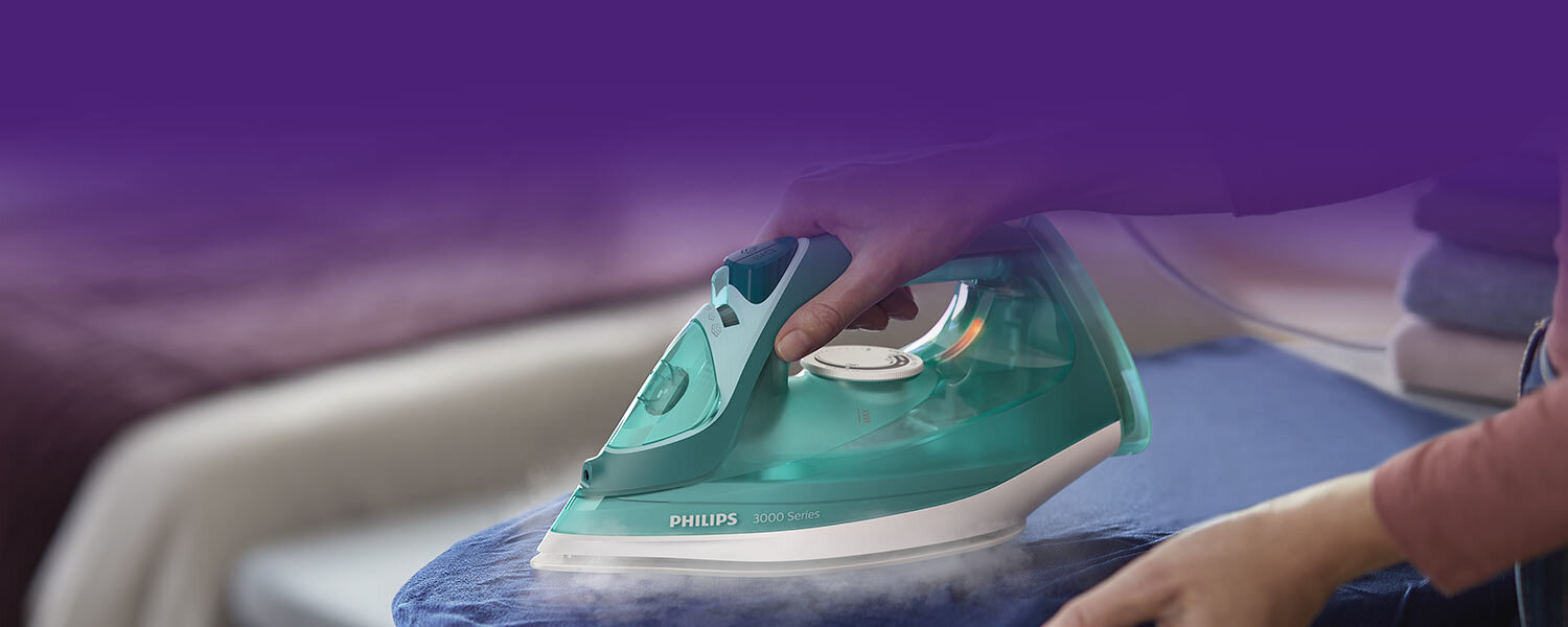 Osoba prasuje niebieski materiał za pomocą zielonego żelazka z napisem \'PHILIPS 3000 Series\'.