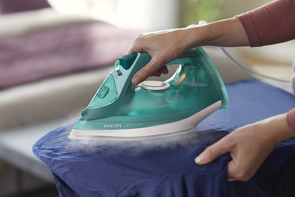 Osoba prasuje niebieski materiał za pomocą żelazka PHILIPS 3000 Series, z którego wydobywa się para. Na żelazku widoczne jest logo \'PHILIPS 3000 Series\'.