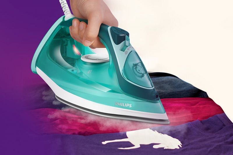 Osoba prasuje kolorową koszulkę żelazkiem w turkusowym kolorze z widocznym logo \'PHILIPS\'. Z żelazka wydobywa się para, a na koszulce widoczny jest biały kształt konia.