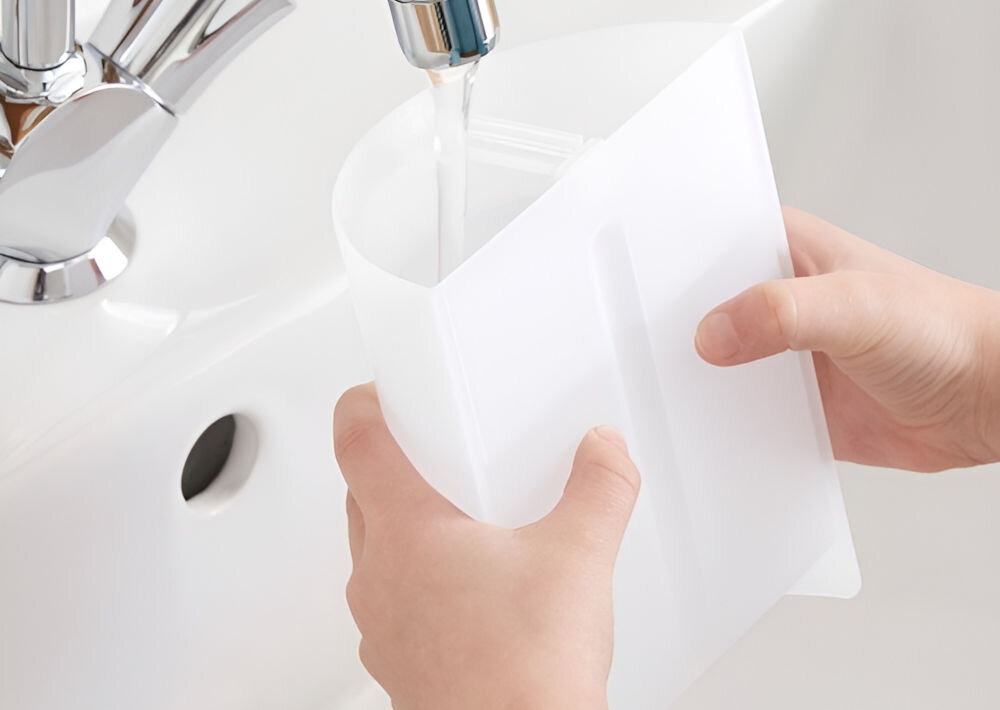 Osoba trzyma biały pojemnik pod kranem, z którego leci woda. Pojemnik jest napełniany wodą nad umywalką.