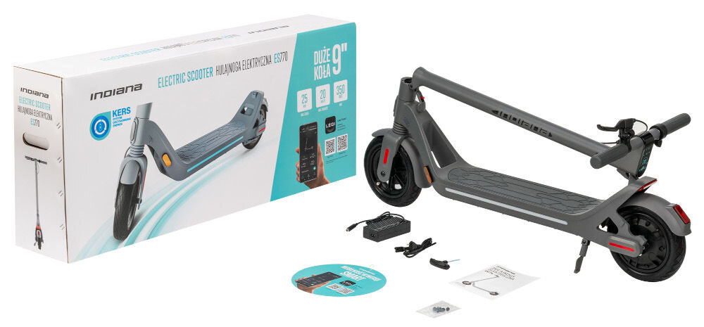 Na obrazie znajduje się szara hulajnoga elektryczna z dużymi kołami, obok której leży pudełko z napisem \'INDIANA ELECTRIC SCOOTER HULAJNOGA ELEKTRYCZNA ES770\'. W zestawie widoczne są również ładowarka, instrukcja oraz inne akcesoria.
