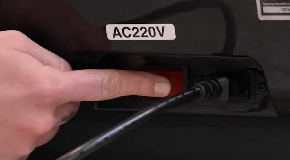 Osoba naciska czerwony przycisk obok wtyczki z napisem \'AC220V\'.