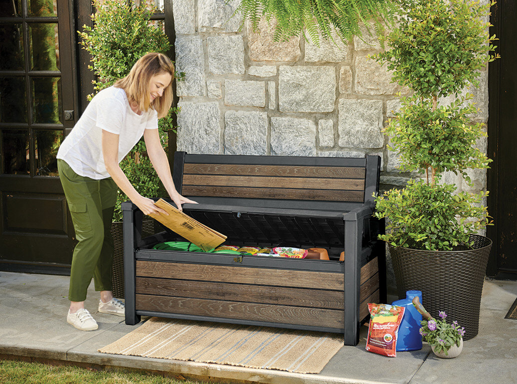 Ławka ogrodowa KETER Deco Garden Bench Brązowy, 227 litrów, wymiary, schowek, organizacja, Kobieta chowa akcesoria ogrodowe do schowka w ławce Deco Garden Bench.