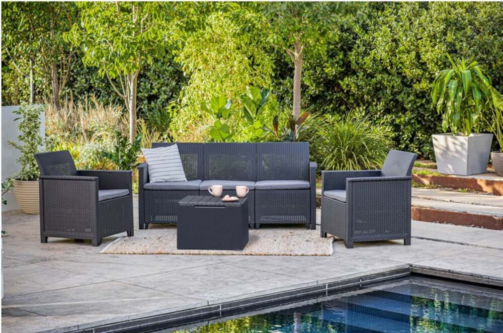 Zestaw mebli ogrodowych składający się z dwóch foteli, sofy i stolika, ustawiony na tarasie przy basenie. Meble są w kolorze grafitowo-jasnoszarym, a w tle widoczna jest bujna roślinność.