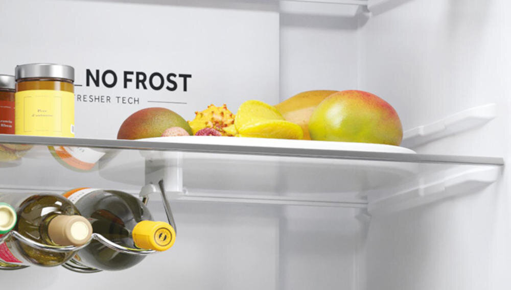 Wnętrze lodówki z półką, na której znajdują się owoce i słoik. Widoczny napis: \'NO FROST FRESHER TECH\'.