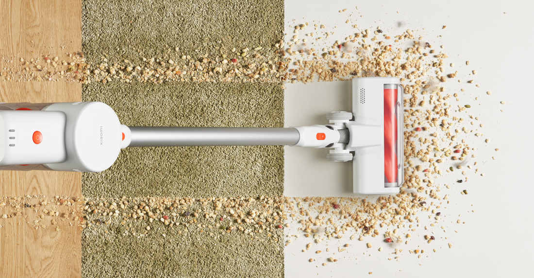 Odkurzacz usuwa rozsypane okruchy z dywanu i podłogi, pozostawiając czystą powierzchnię. Widoczny jest biały odkurzacz z czerwonymi elementami.