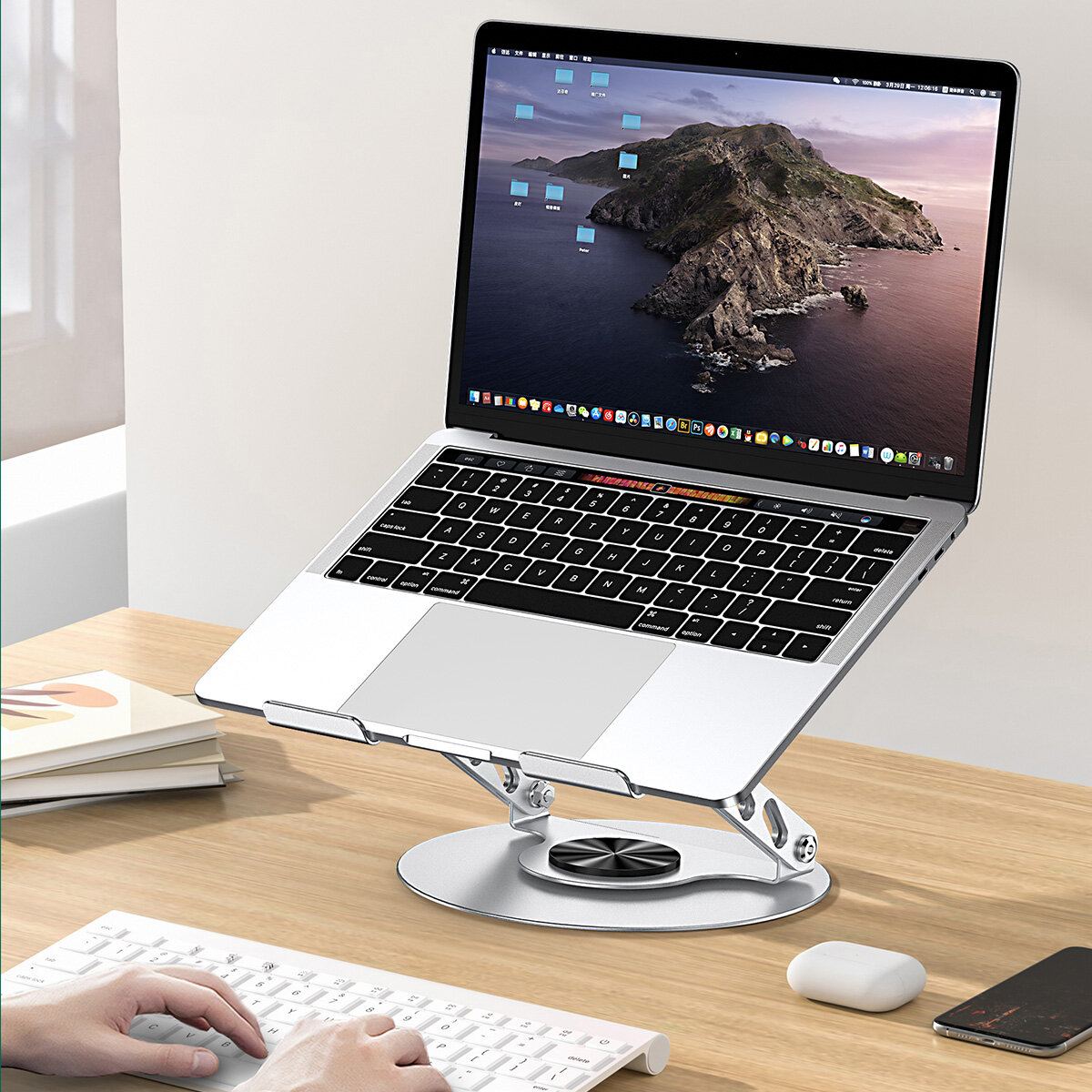 Na drewnianym biurku znajduje się laptop umieszczony na srebrnej, regulowanej podstawce z wentylatorem. Obok klawiatury widoczne są dłonie osoby piszącej.