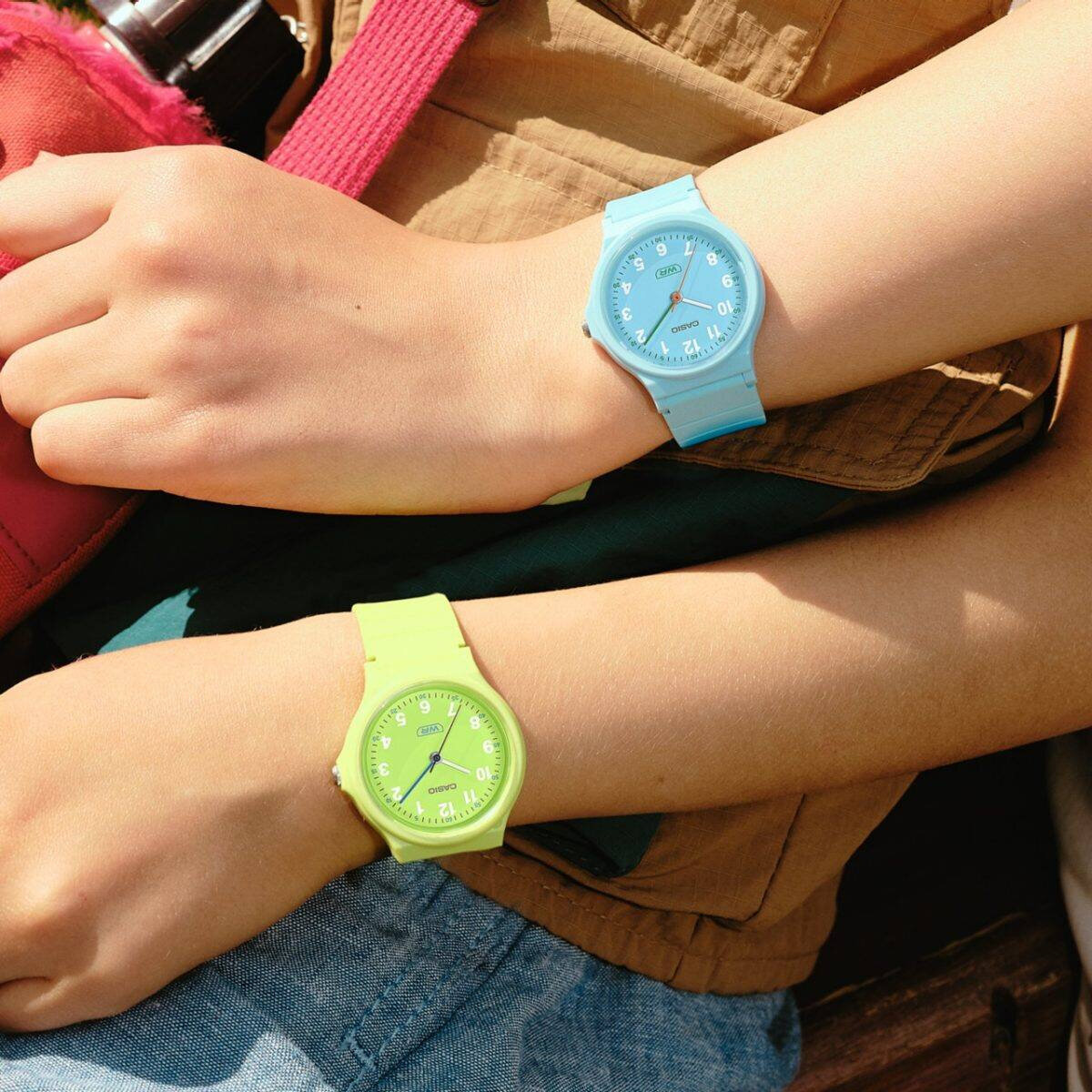 Na zdjęciu widoczne są dwa zegarki na nadgarstkach, jeden w kolorze niebieskim, drugi w kolorze zielonym. Oba zegarki mają okrągłe tarcze z widocznym logo Casio i cyframi arabskimi.
