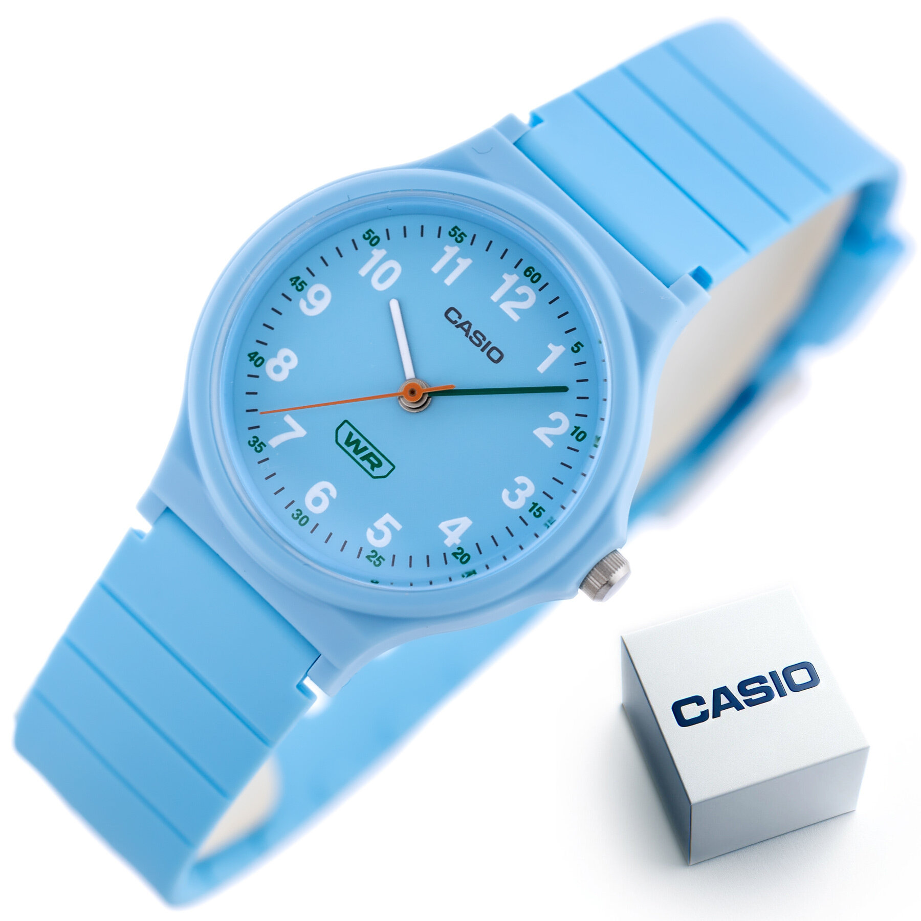 Jasnoniebieski zegarek z białymi cyframi i wskazówkami oraz zielonym napisem \'WR\' na tarczy. Obok zegarka znajduje się pudełko z napisem \'CASIO\'.