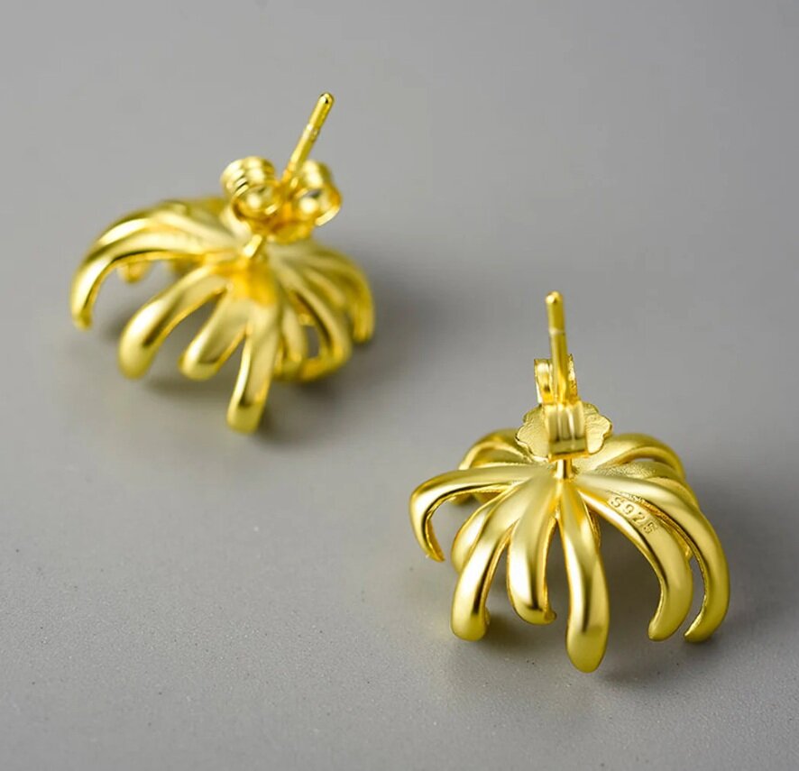 Na obrazie widoczne są dwa złote kolczyki o kształcie przypominającym chryzantemę, wykonane z pozłacanego srebra. Na jednym z kolczyków widoczny jest napis \'S925\'.