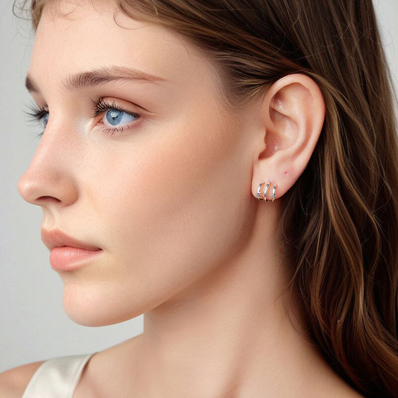 Na zdjęciu widoczne są srebrne kolczyki w kształcie potrójnych obręczy na uchu osoby. Kolczyki mają delikatny, elegancki wygląd.