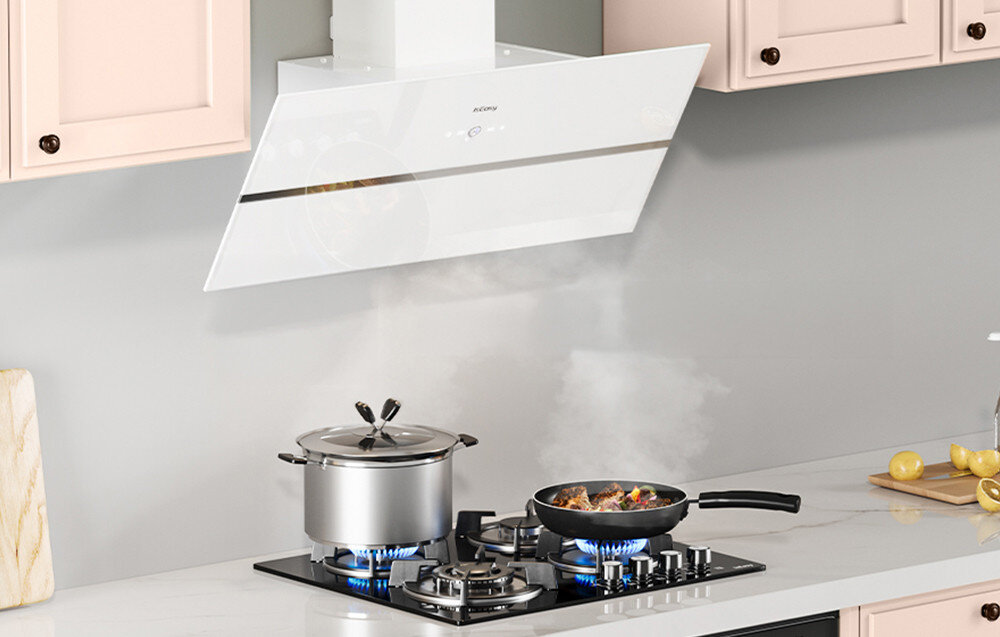 Na obrazie widoczny jest biały okap kuchenny z logo \'ISEASY\' zamontowany nad płytą gazową, na której stoją dwa garnki z gotującymi się potrawami. W tle znajdują się jasne szafki kuchenne i szary blat z cytrynami.