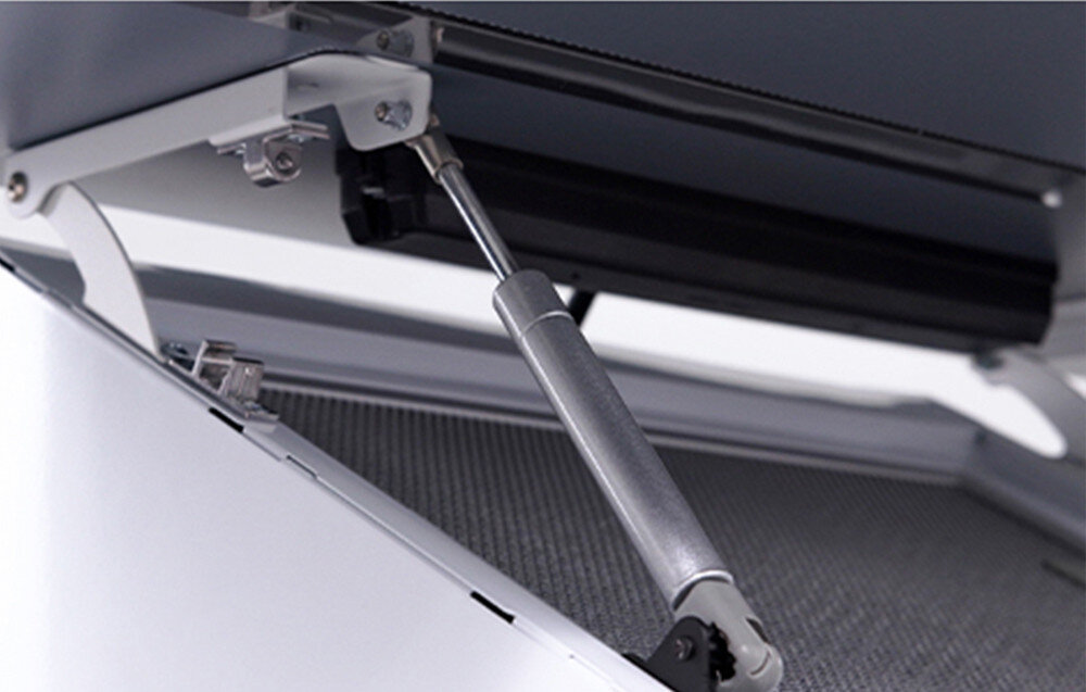 Zbliżenie na mechanizm teleskopowy okapu kuchennego z metalowym ramieniem i siłownikiem. W tle widoczna jest metalowa siatka filtracyjna.