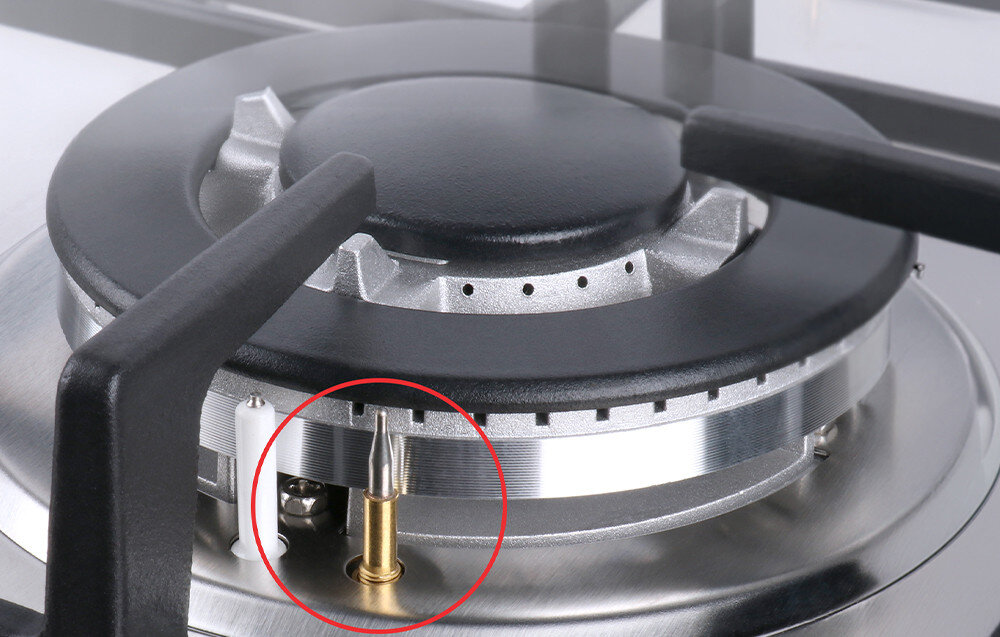 Zbliżenie na palnik płyty gazowej z metalowym rusztem i elementem zapłonowym zaznaczonym czerwonym okręgiem. Palnik wykonany jest z metalu i ma czarną pokrywę.