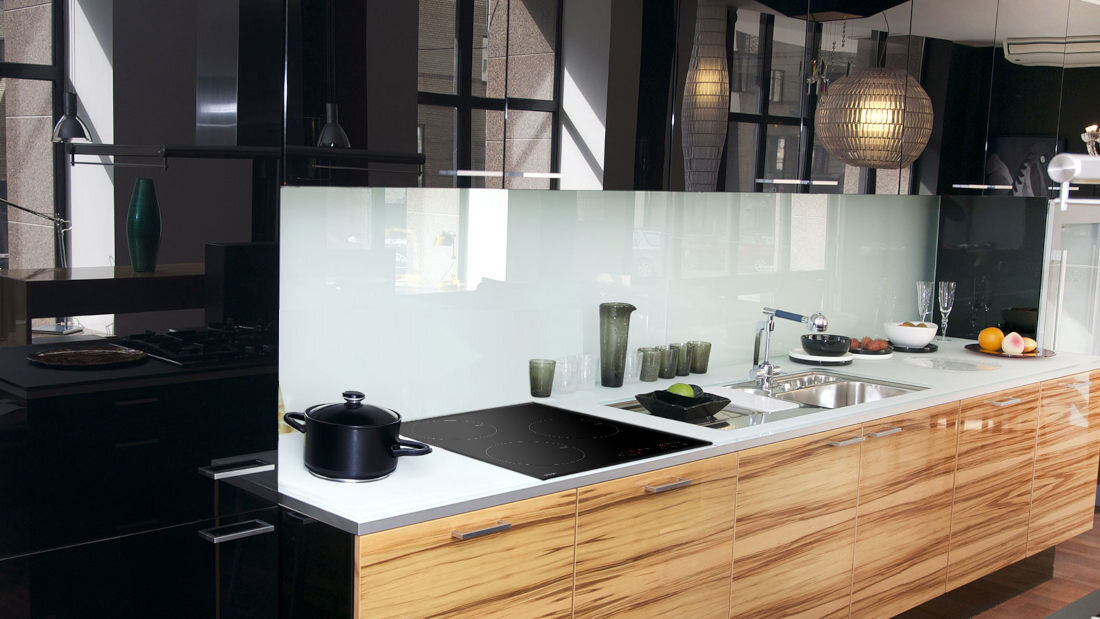 Nowoczesna kuchnia z drewnianymi szafkami i białym blatem, na którym znajduje się czarna płyta indukcyjna. Obok płyty stoi czarny garnek, a w tle widać zlew i różne naczynia.