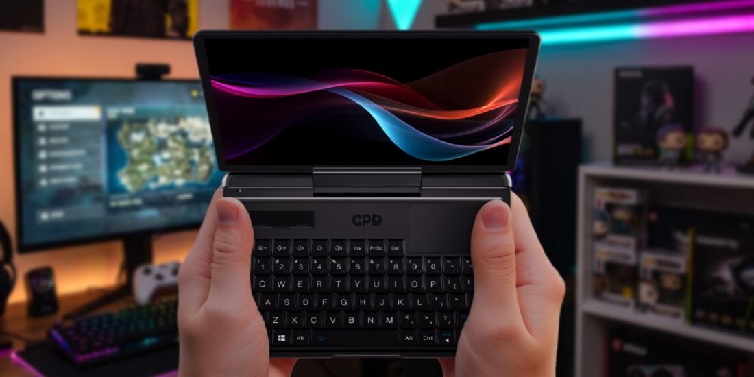Osoba trzyma mały laptop z otwartym ekranem, na którym widoczna jest kolorowa grafika. Na obudowie laptopa znajduje się logo \'GPD\'.