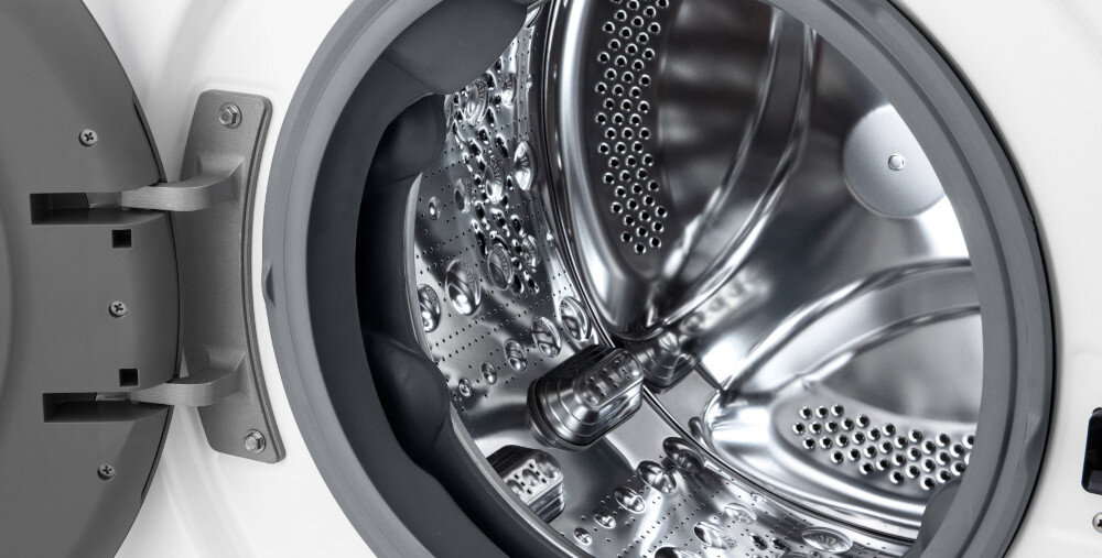 Zdjęcie przedstawia wnętrze bębna pralki z metaliczną powierzchnią i otworami. Drzwi pralki są otwarte, ukazując szczegóły konstrukcji bębna.