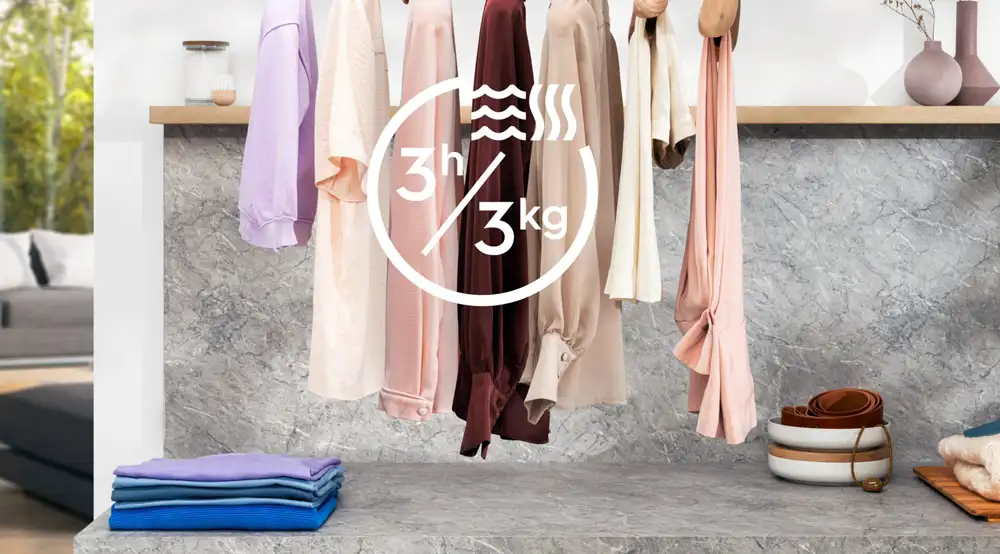 Na obrazie widoczne są różnokolorowe ubrania wiszące na wieszaku oraz złożone ręczniki na marmurowym blacie. Na środku znajduje się symbol z tekstem \'3h/3kg\'.