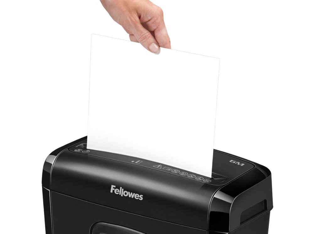 Osoba wkłada kartkę papieru do czarnej niszczarki z widocznym logo \'Fellowes\'. Na panelu urządzenia znajdują się różne ikony i oznaczenie \'6M\'.