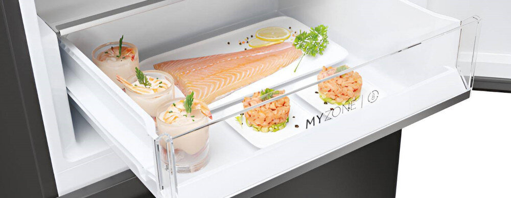 Otwarta szuflada lodówki z napisem \'MY ZONE\', w której znajdują się potrawy, w tym kawałek surowego łososia i przystawki w małych naczyniach.