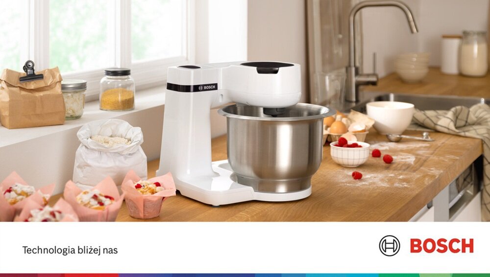 Na blacie kuchennym znajduje się biały robot kuchenny z metalową misą, obok którego leżą składniki do pieczenia. Na dole obrazu widnieje napis \'Technologia bliżej nas\' oraz logo BOSCH.