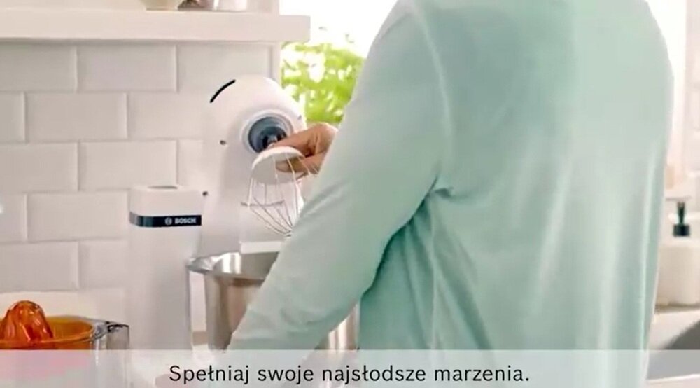 Osoba obsługuje biały robot kuchenny marki BOSCH w kuchni. Na dole obrazu widnieje tekst: \'Spełniaj swoje najsłodsze marzenia.\'