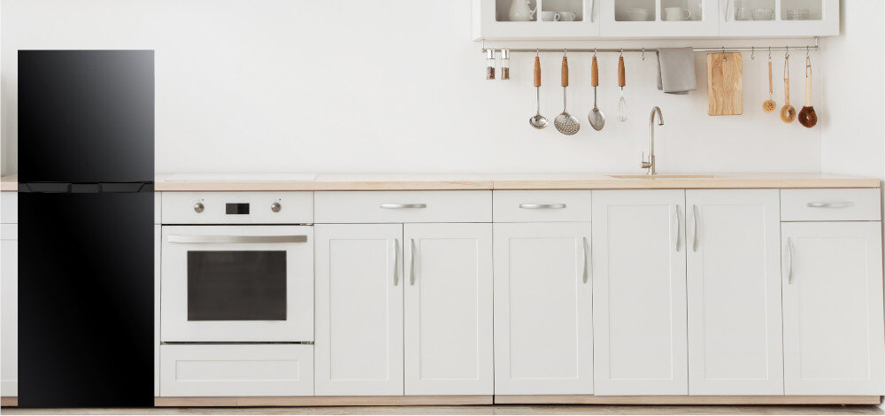 Kuchnia z białymi szafkami i czarną lodówką. Nad blatem wiszą przybory kuchenne, a na blacie znajduje się zlew i piekarnik.