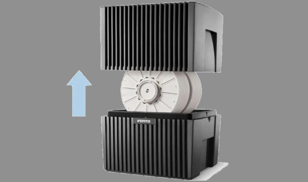 Obraz przedstawia nawilżacz ewaporacyjny w kolorze antracytowym z widocznym logo \'venta\'. Urządzenie jest rozłożone, ukazując wewnętrzny mechanizm z białym elementem obrotowym oraz niebieską strzałką wskazującą kierunek ruchu.