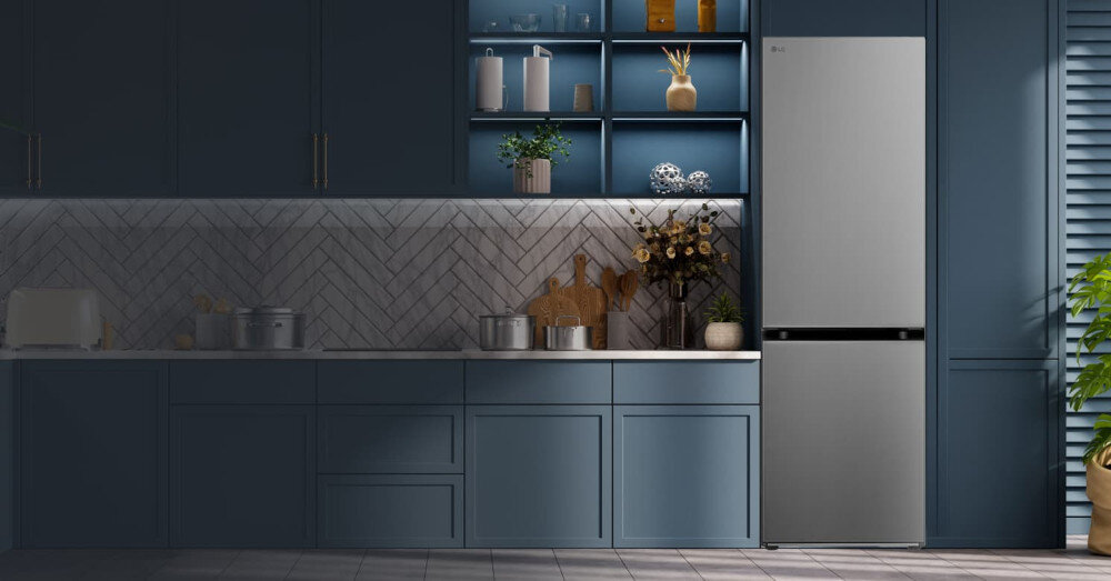 Kuchnia z niebieskimi szafkami i srebrną lodówką LG. Na blacie znajdują się garnki, deski do krojenia i dekoracje roślinne.