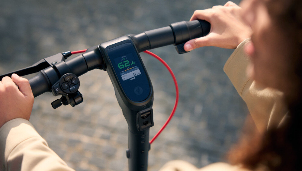 Hulajnoga elektryczna SEGWAY Ninebot F3 Pro D 70km 1200W Amortyzacja 10 cali Czarny chodnik zbliżenie na kierownicę kierownica z włączonym wyświetlaczem osoba trzyma dłonie na uchwytach kierownicę o wysokości 126 cm podróżowanie w wyprostowanej pozycji ciała 2,4-calowy wyświetlacz TFT wysoka rozdzielczość