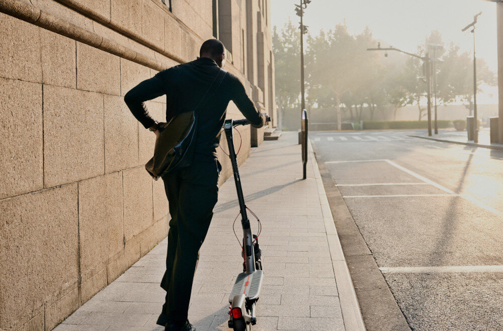 Hulajnoga elektryczna SEGWAY Ninebot F3 Pro D 70km 1200W Amortyzacja 10 cali Czarny miasto osoba prowadzi hulajnogę po drodze budynki drzewa niebo 3 tryby jazdy tryb pieszy prędkość do 6 km/h tryb ECO prędkość do 15 km/h tryb SPORT MODE prędkość do 20 km/h