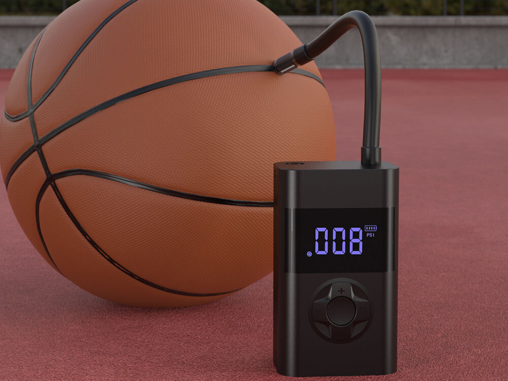 Na obrazie widoczna jest pompka rowerowa z wyświetlaczem pokazującym \'.008 PSI\', obok której znajduje się piłka do koszykówki. Pompka ma ciemny kolor i elastyczny wąż podłączony do piłki.
