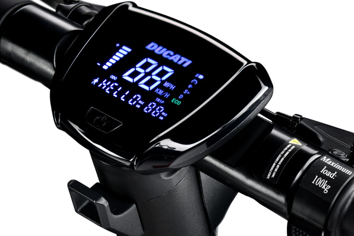 Zbliżenie na wyświetlacz hulajnogi elektrycznej z logo \'DUCATI\' i cyfrowym prędkościomierzem pokazującym \'88\'. Obok znajduje się napis \'Maximum load: 100kg\'.