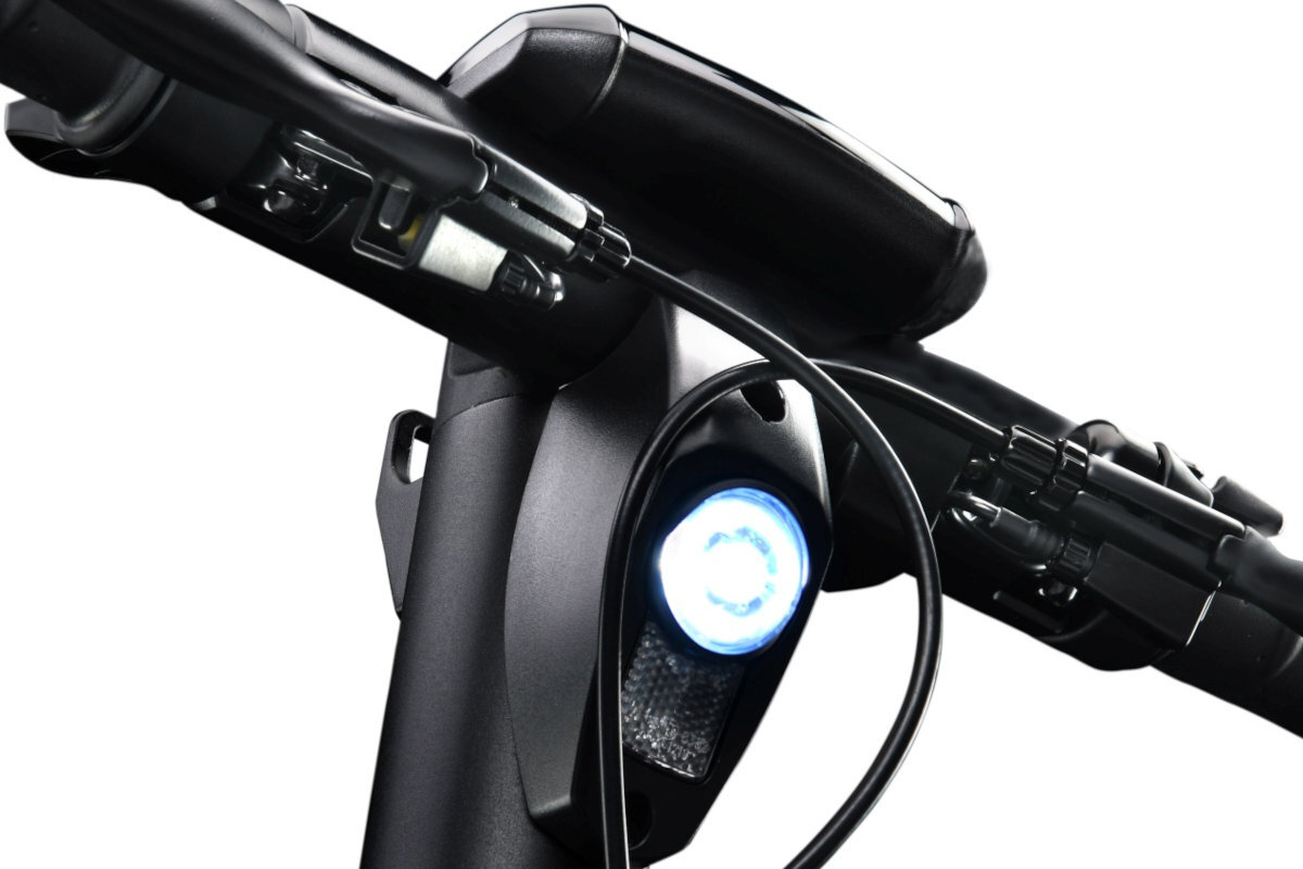 Zbliżenie na kierownicę hulajnogi elektrycznej z widocznym reflektorem emitującym jasne światło. W tle widać elementy konstrukcyjne i przewody.