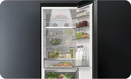 Otwarta lodówka z widocznymi półkami, na których znajdują się różne produkty spożywcze w słoikach i butelkach. Na drzwiach lodówki umieszczone są dodatkowe półki z napojami i słoikami.