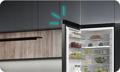 Otwarta lodówka z widocznymi półkami wypełnionymi jedzeniem, w tym warzywami i napojami. W tle widoczne są szafki kuchenne.