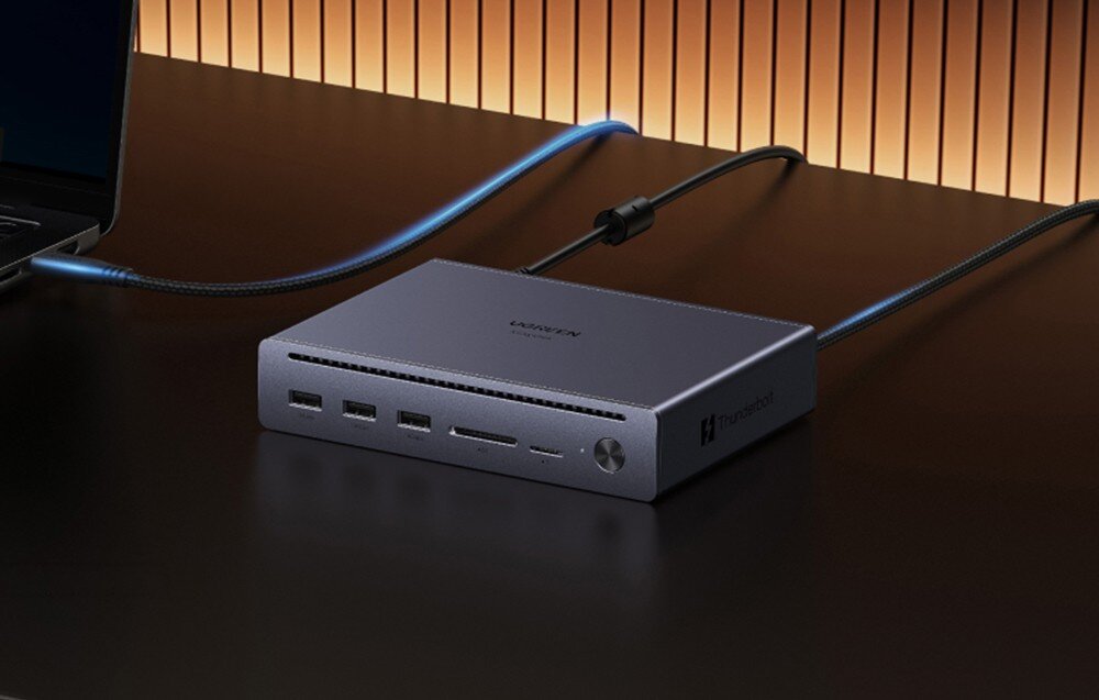 Stacja dokująca UGREEN Maxidok U712 Stacja dokująca na ciemnym biurku połączona kablem z laptopem, widoczne czytniki kart i porty USB