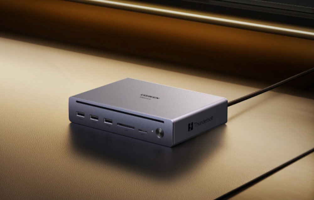 Stacja dokująca UGREEN Maxidok U712 Szara stacja dokująca Ugreen Thunderbolt leżąca na blacie biurka w ciepłym, nastrojowym oświetleniu.