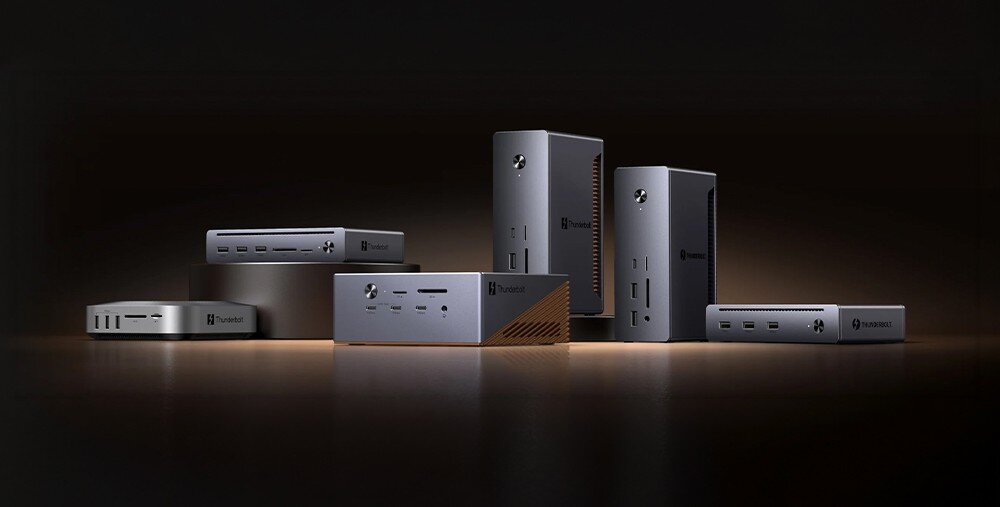 Na obrazie widoczne są różne modele stacji dokujących w kolorze szarym z logo \'Thunderobot\'. Produkty są ustawione na ciemnym tle z delikatnym oświetleniem od dołu.
