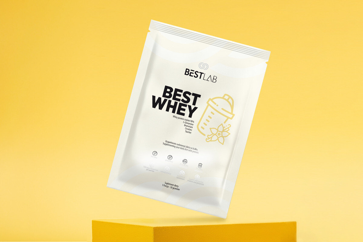 Na żółtym tle widoczna jest saszetka z napisem \'BESTLAB BEST WHEY\'. Obok napisu znajduje się grafika shakera z kwiatem wanilii.