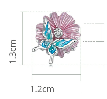 Charms w kształcie motyla z niebieskimi skrzydłami na tle różowego kwiatu. Wymiary to 1.3 cm na 1.2 cm.