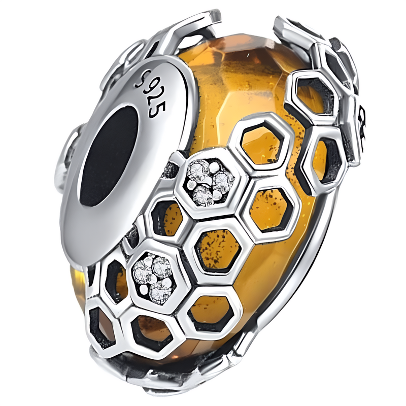 Zawieszka charms o miodowym kolorze z motywem plastrów miodu, wykonana z metalu z oznaczeniem \'S925\'. Elementy w kształcie sześciokątów zawierają małe, błyszczące kamienie.