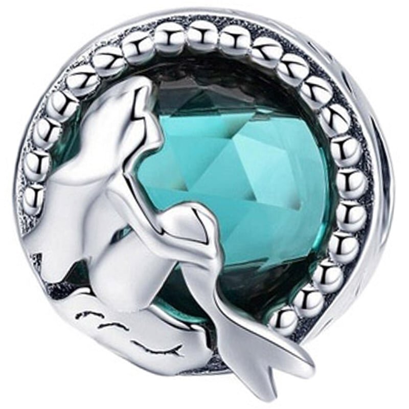 Srebrny charms przedstawiający syrenę siedzącą przed dużym, błękitnym kryształem. Wokół kryształu znajduje się ozdobna ramka z małymi, metalicznymi kulkami.