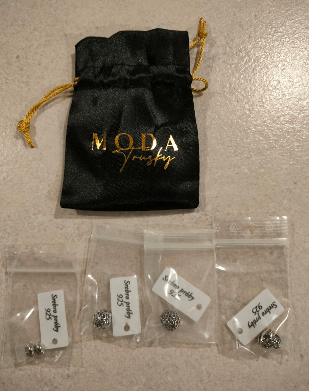 Na obrazie widoczny jest czarny woreczek z napisem \'MODA Trusky\' oraz cztery przezroczyste woreczki strunowe z zawieszkami i etykietami \'Srebro próby 925\'.