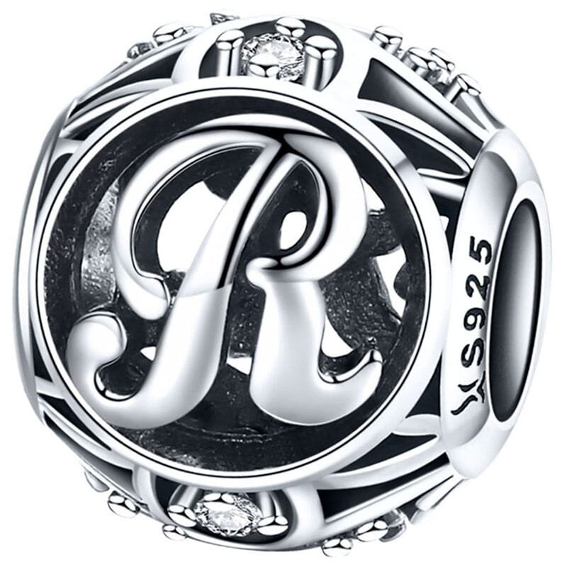 Srebrna zawieszka charms z literą \'R\' ozdobiona drobnymi kamieniami. Na boku widoczny jest napis \'S925\'.