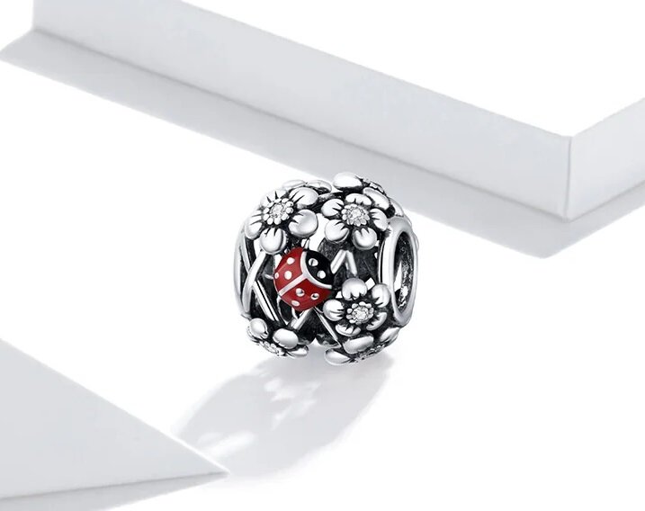 Ażurowa zawieszka charms z motywem kwiatów i czerwonej biedronki. Wykonana z metalu, z detalami w kształcie kwiatów i małej biedronki na powierzchni.