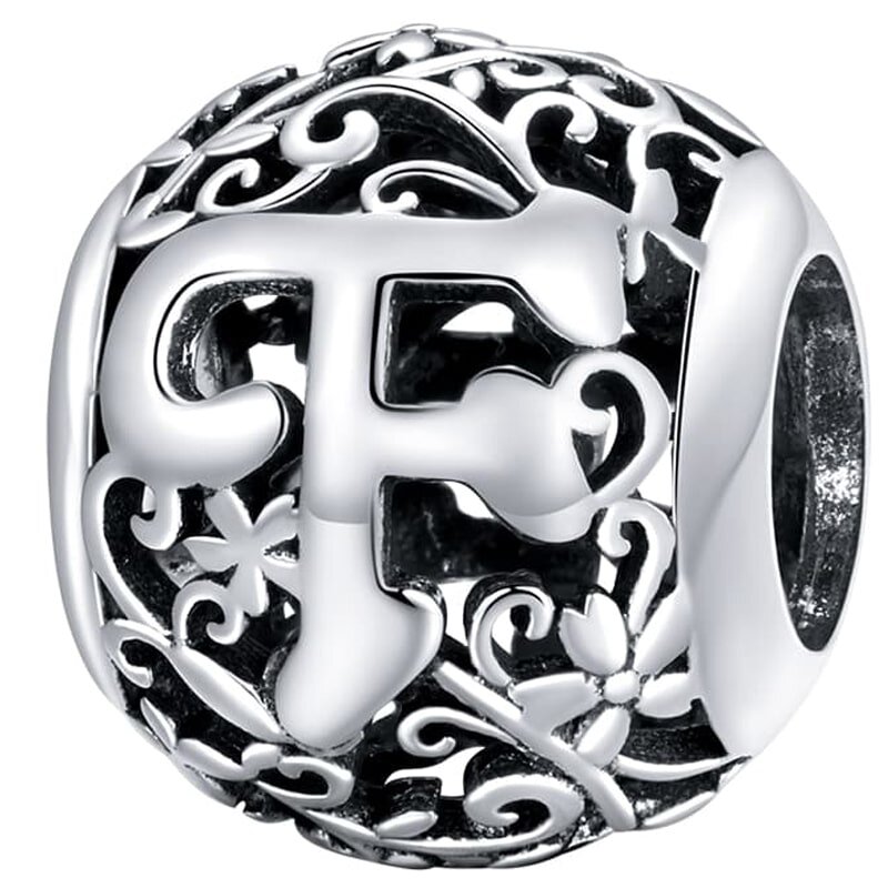 Srebrna zawieszka charms z literą \'F\' otoczona ozdobnymi wzorami kwiatowymi i spiralnymi. Powierzchnia jest błyszcząca i szczegółowo zdobiona.